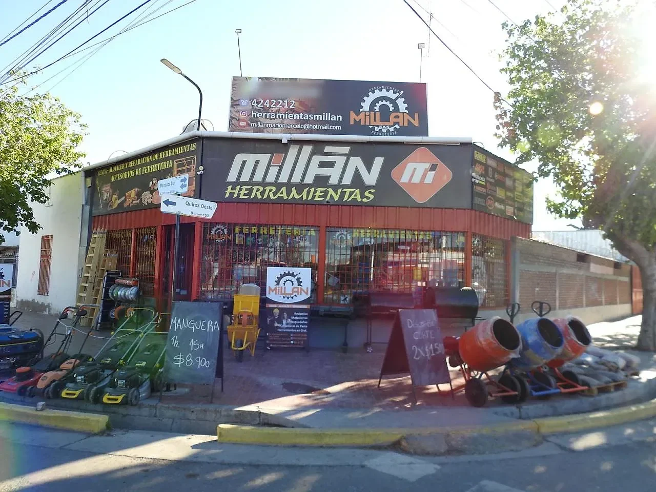 Frente del local de día, en la esquina, con el cartel de Millán Herramientas y máquinas exhibidas en la vereda