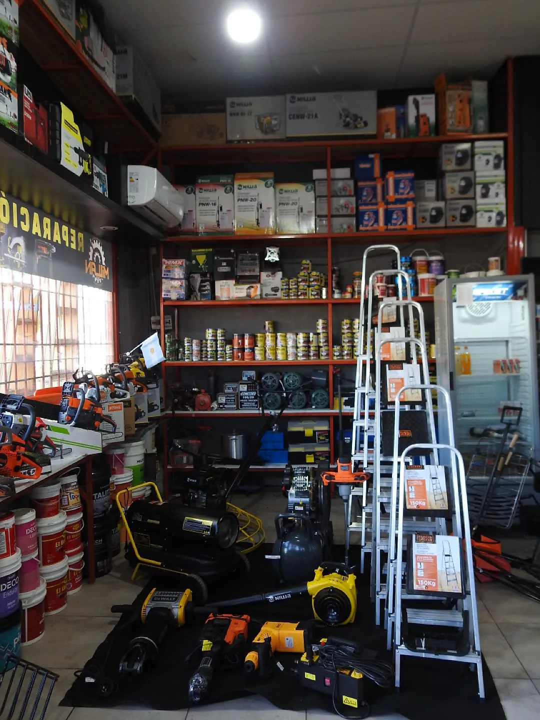 Estantería del salón con herramientas, escaleras de aluminio y máquinas en el piso